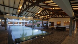 A large indoor swimming pool with a wooden deck surrounding it, under a high ceiling with exposed beams. - The Beach Boutique Hotel (Uswetakeiyawa)