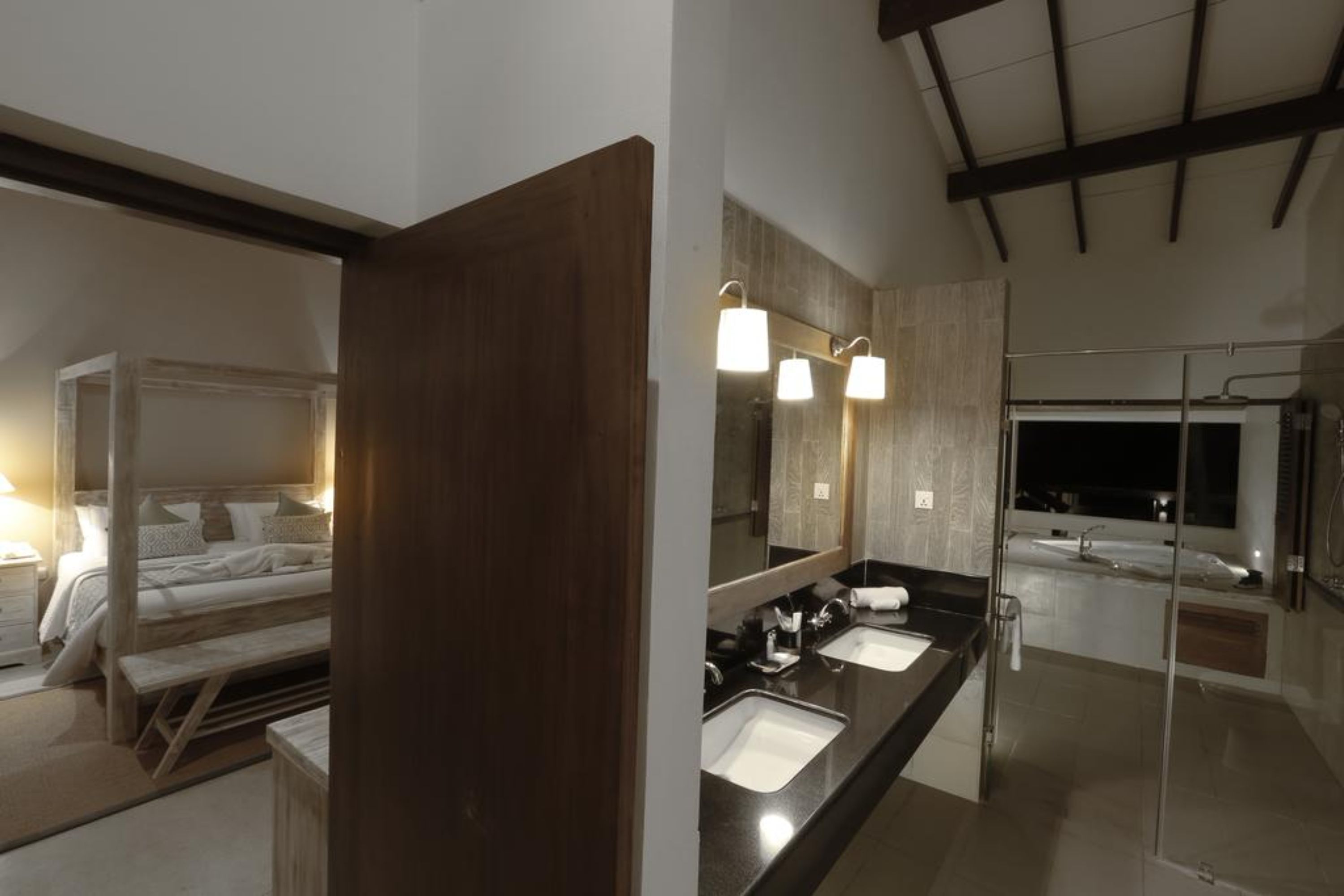 A modern hotel room with a large bed, a separate sitting area, a bathroom with a large mirror, two sinks, and a bathtub.