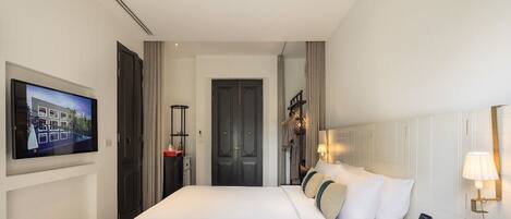 A modern hotel room with a large bed, a TV mounted on the wall, a bedside table, and a lamp.