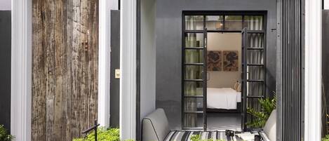 Un edificio moderno con un amplio puertas corredera que da a un dormitorio con cama, un pequeño rincón de descanso y vistas al jardín.