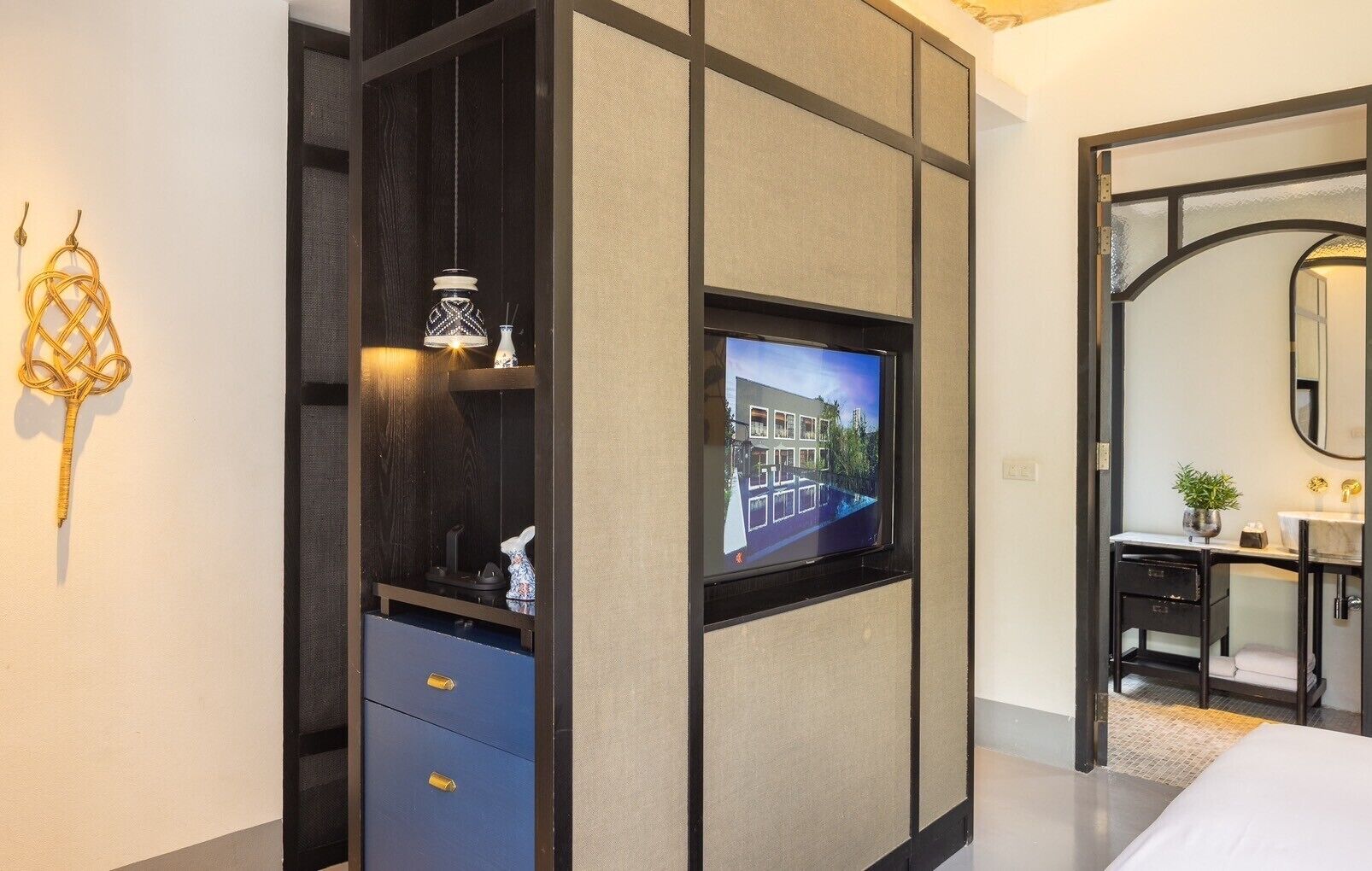 A modern hotel room with a TV mounted on a wall, a wardrobe with a mirror, and a bathroom with a vanity and mirror.
