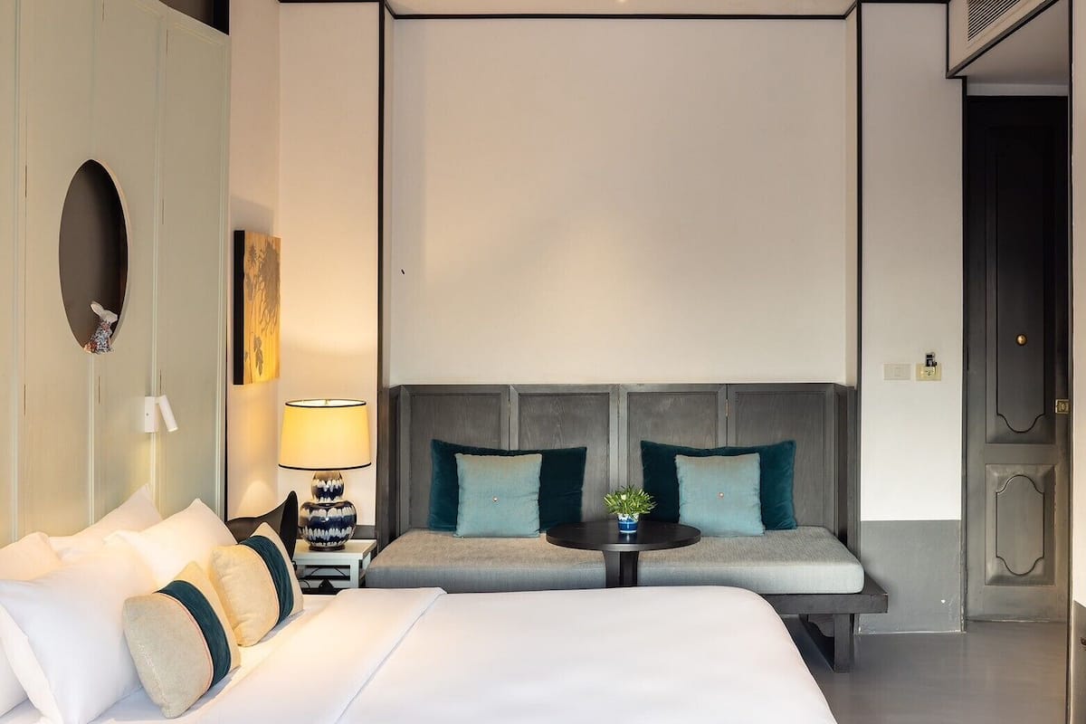 Una habitación de hotel moderna con una cama grande, un sofá, una mesita y un televisor instalado en la pared.
