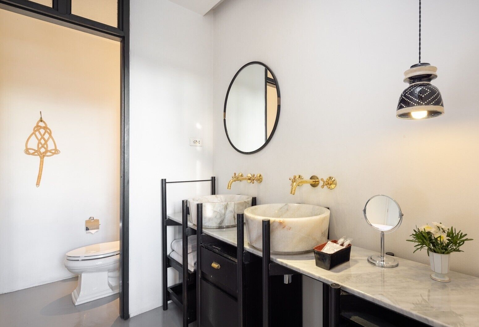 Une salle de bain moderne avec un lavabo en marbre, des robinetteries dorées, un miroir rond et un luminaire suspendu.