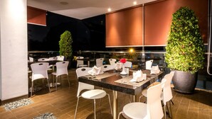A modern indoor dining area with a black marble table, white chairs, and a large potted plant. - Redstar Hotel (Jakarta)
