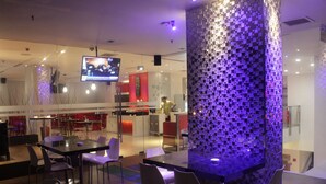 A modern restaurant with a central dining area featuring a black table and white chairs, surrounded by a mosaic-tiled column. - Redstar Hotel (Jakarta)