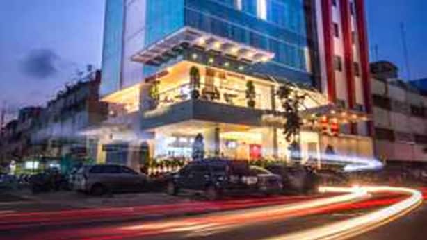 A modern hotel with a glass facade, multiple floors, and a prominent red and white structure to the right. - Redstar Hotel (Jakarta)
