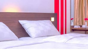 Une chambre d’hôtel avec une tête de lit en bois, une literie blanche et une table de chevet sur laquelle se trouvent une lampe et un vase de fleurs.