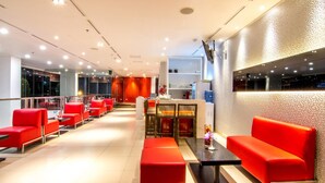 A modern hotel lobby with red seating, a reception desk, and a large mirror on the wall. - Redstar Hotel (Jakarta)