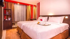 A hotel room with a large bed, a bedside table, a nightstand, and a shelf with a lamp and a book. - Redstar Hotel (Jakarta)
