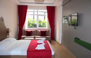 A hotel room with a bed, a bench, a window with curtains, a plant, and a mounted TV. - Almond Hill Apart (Istanbul)