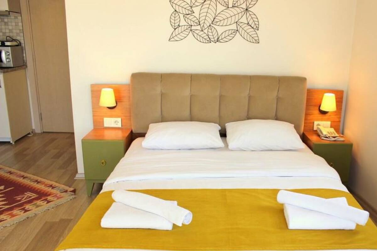 A neatly made bed with white linens and two pillows, flanked by two bedside tables with lamps, in a room with a simple decor and a wall art piece above the bed.