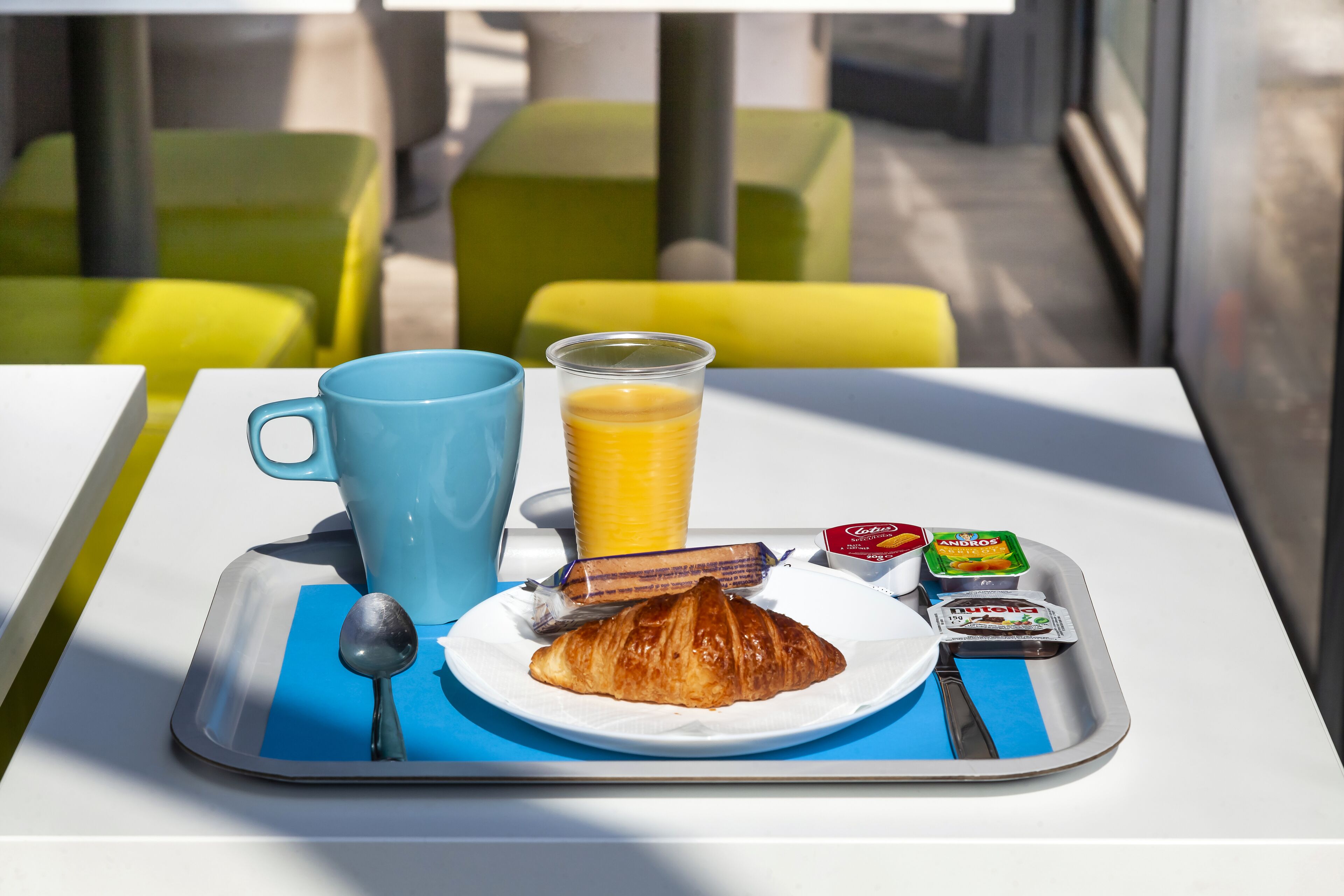 Een ontbijfwagen met een croissant, sap en toevoegingen op een tafel met een blauwe placemat.