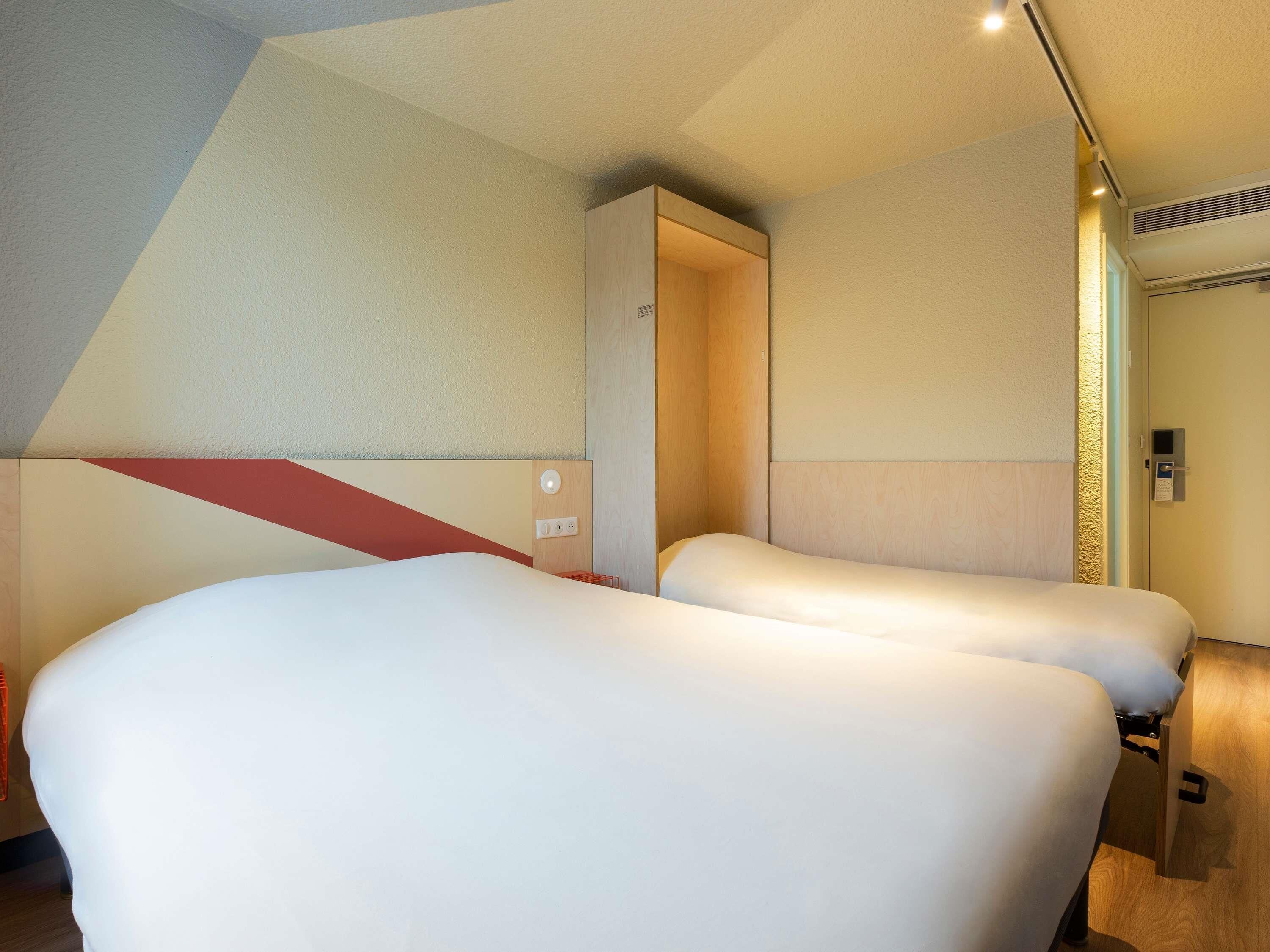 A modern hotel room with two beds, a wooden wardrobe, and a built-in heater.