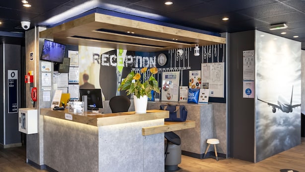 A reception area with a wooden counter, a potted plant, and informational posters. - ibis Budget Antony Massy (renovated 2024) (Antony)