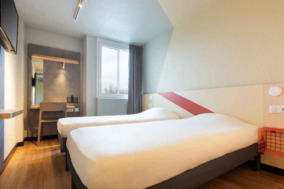 A hotel room with two beds, a desk, and a window.