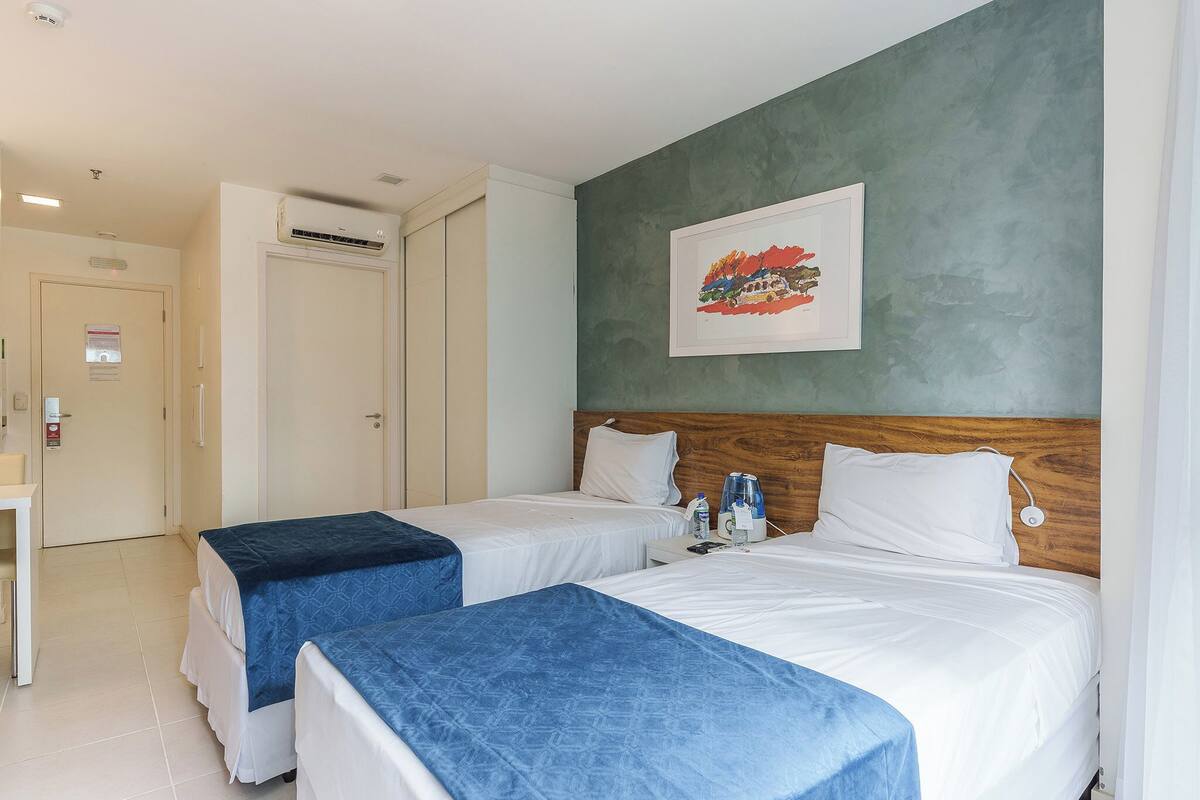 A hotel room with two beds, a desk, and a bathroom.