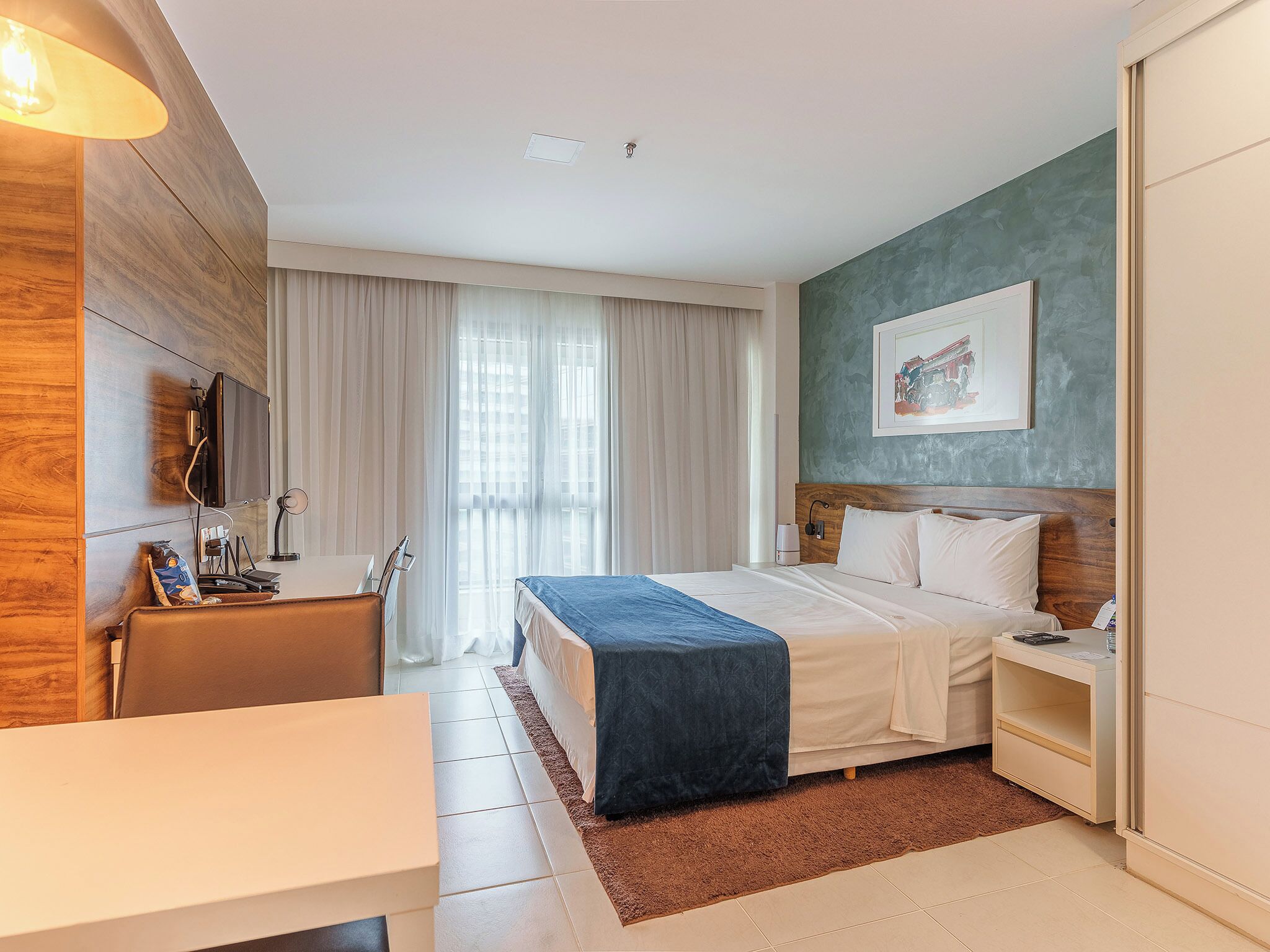 Una habitación de hotel moderna con cama, mesita de noche, escritorio y televisor montado en la pared.