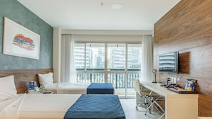 A hotel room with a bed, a desk, a television, and a view of the city. - Hplus Vision Executive (Brasília)