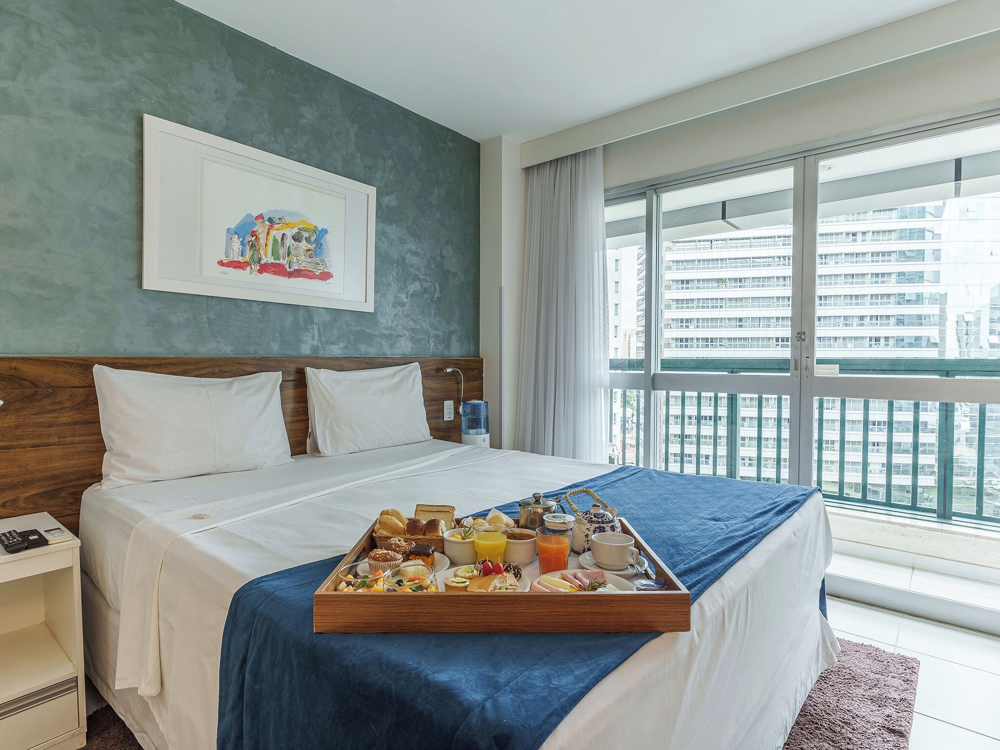 Habitación de hotel con cama, bandeja de desayuno, mesita de noche, teléfono y ventana con vista a la ciudad.