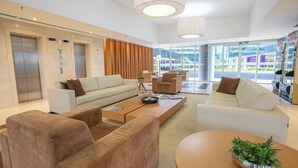 A modern lobby with two elevators, a white sofa, a coffee table, and a view of the outside. - Hplus Vision Executive (Brasília)