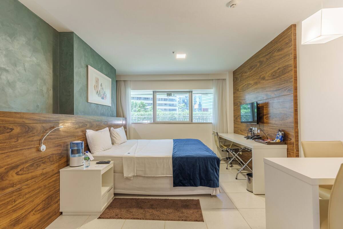A modern hotel room with a bed, bedside table, desk, and TV.