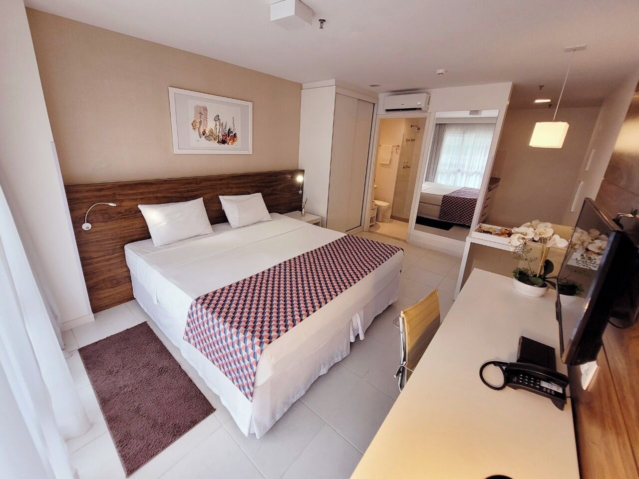 Quarto de hotel com uma cama grande, uma escrivaninha com telefone e um espelho.