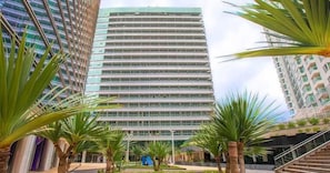 A modern high-rise hotel with a central atrium, surrounded by palm trees and other greenery. - Hplus Vision Executive (Brasília)