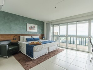 Une chambre d’hôtel moderne, dotée d’un grand lit, d’une table de chevet, d’une chaise et offrant une vue sur la ville grâce à de grandes fenêtres.