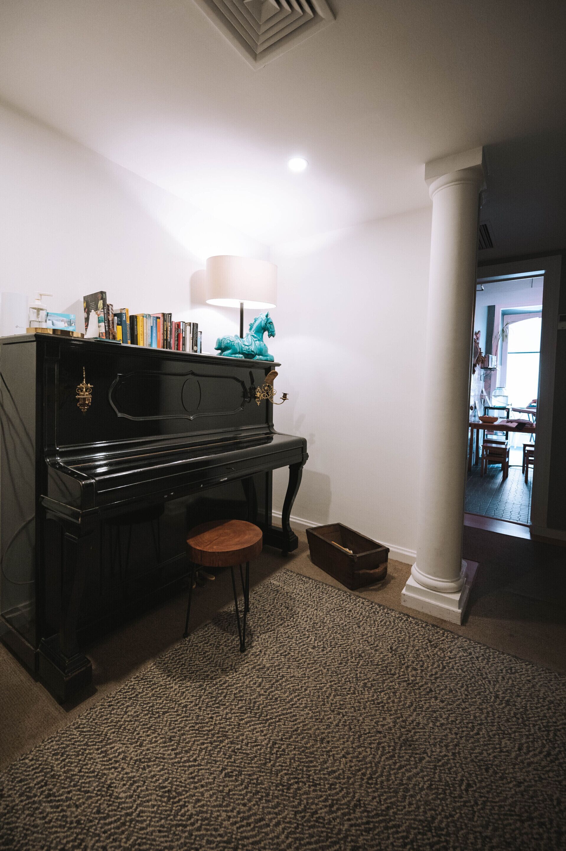 A black piano with a stool in a room with white walls and a carpeted floor.