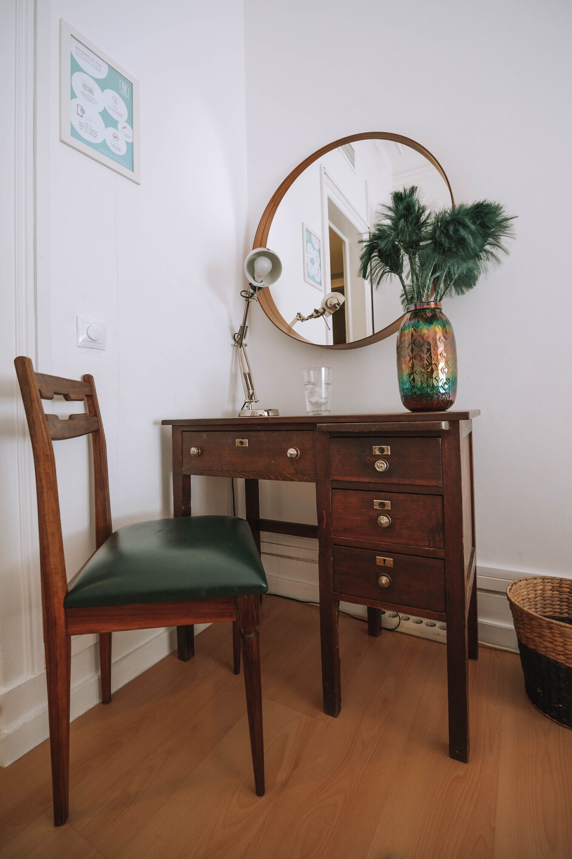 Un bureau en bois avec un miroir, une chaise verte et un vase décoratif contenant une plante.