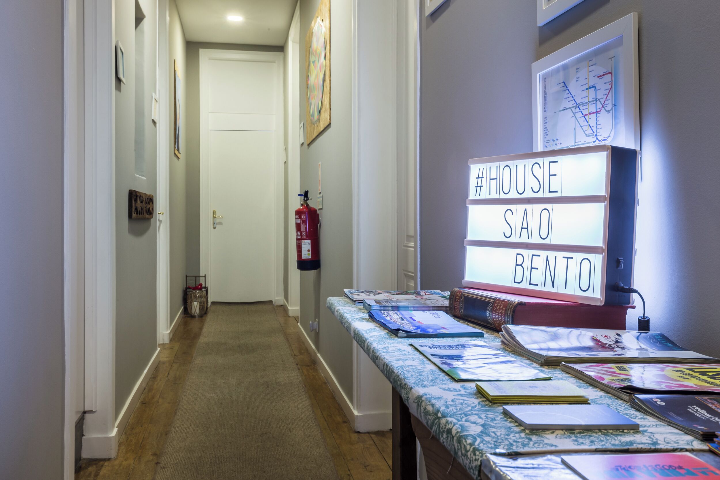 A hallway with a table displaying books and a sign reading "#HOUSE SAO BENTO".