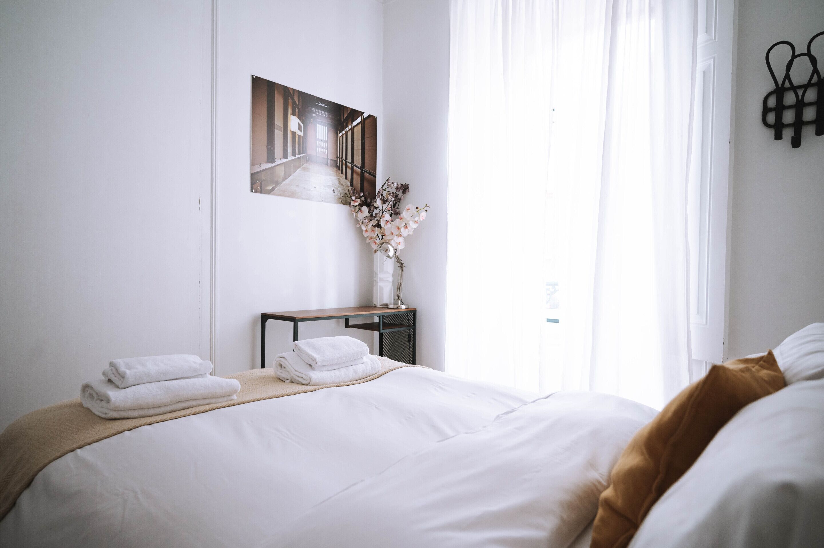 Ein Hotelzimmer mit einem ordentlich bezogenen Bett, einem kleinen Tisch mit Blumen und einem Bild an der Wand.