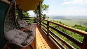 Una terraza de madera con sillas de mimbre y vistas a un paisaje verde.