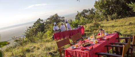 A dining table set with red checkered tablecloths, surrounded by wooden chairs, overlooking a scenic view of the sea.