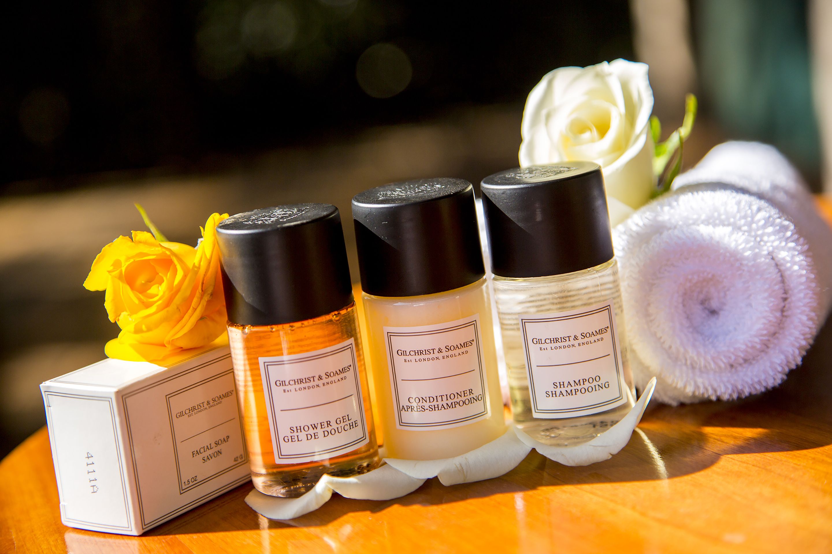 Trois flacons de produits Gilchrist & Soames, une boîte blanche et une rose blanche.