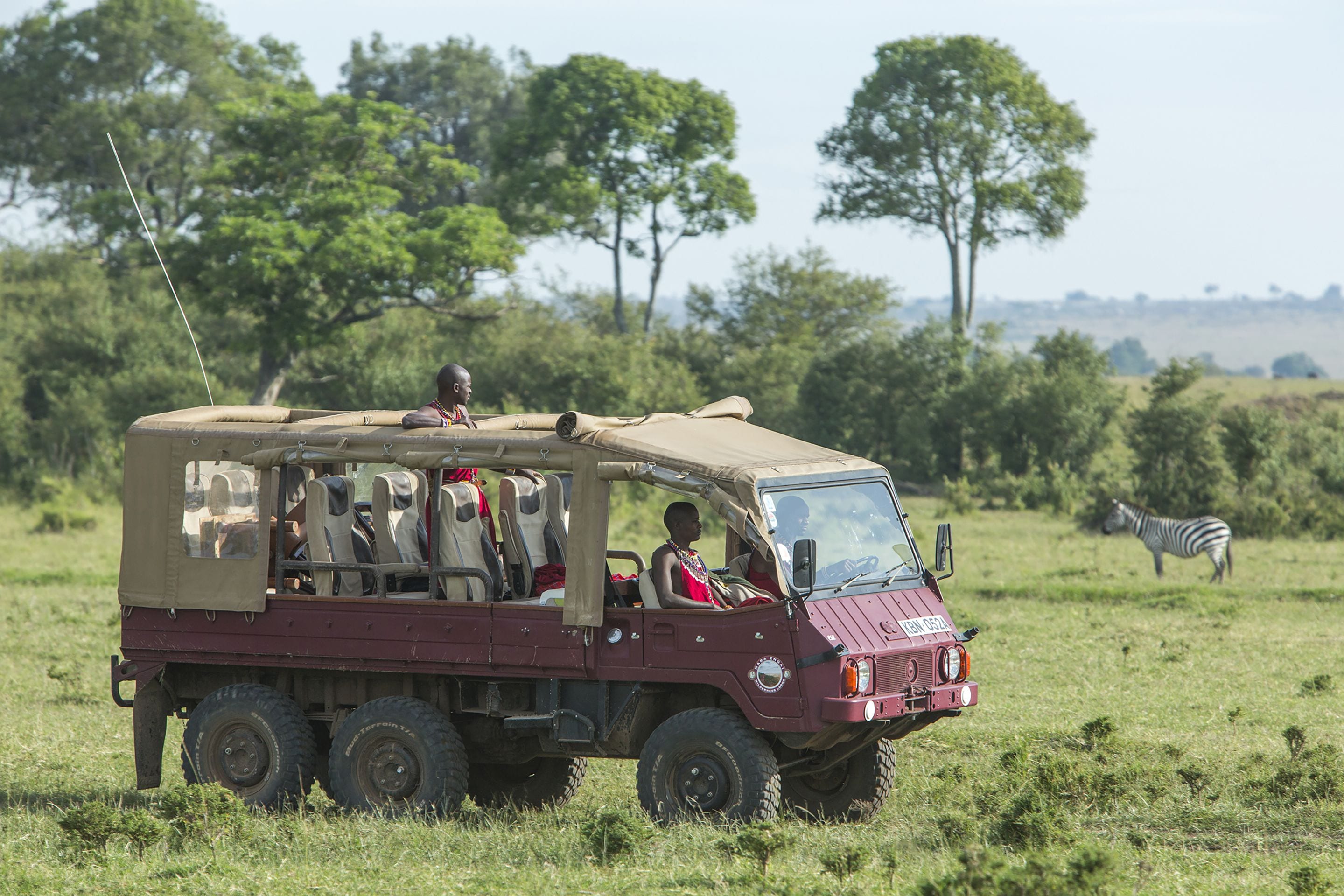 Un véhicule de safari transportant des passagers, une zèbre en arrière-plan et une vue dégagée sur le paysage environnant.