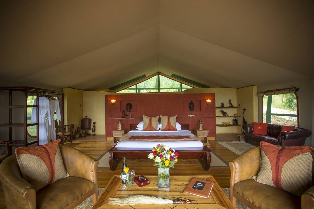 A spacious bedroom with a large bed, a sitting area with leather chairs, a wooden coffee table, and a vase of flowers.