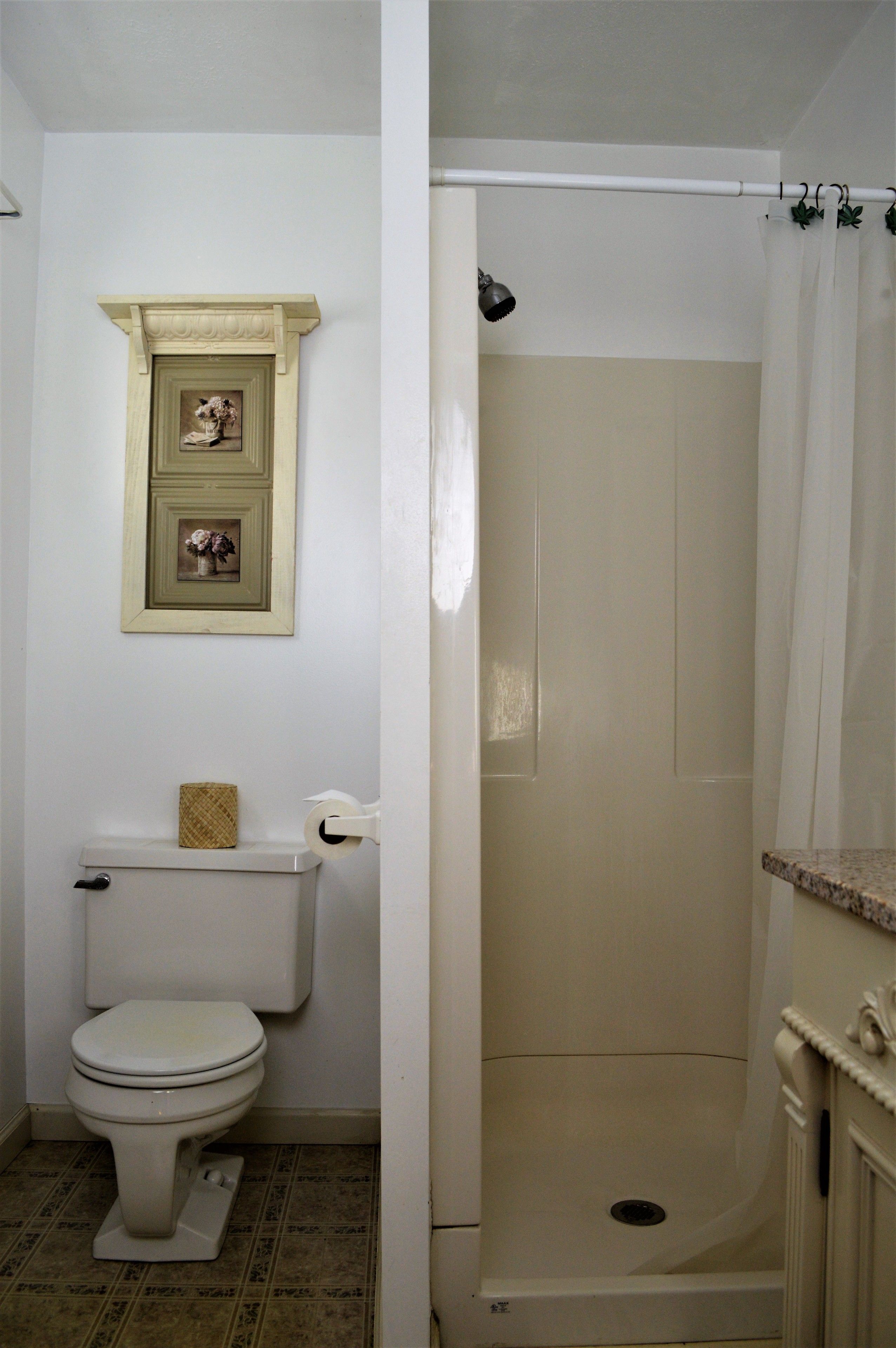 Un baño con inodoro, ducha y un estante decorativo sobre el inodoro.