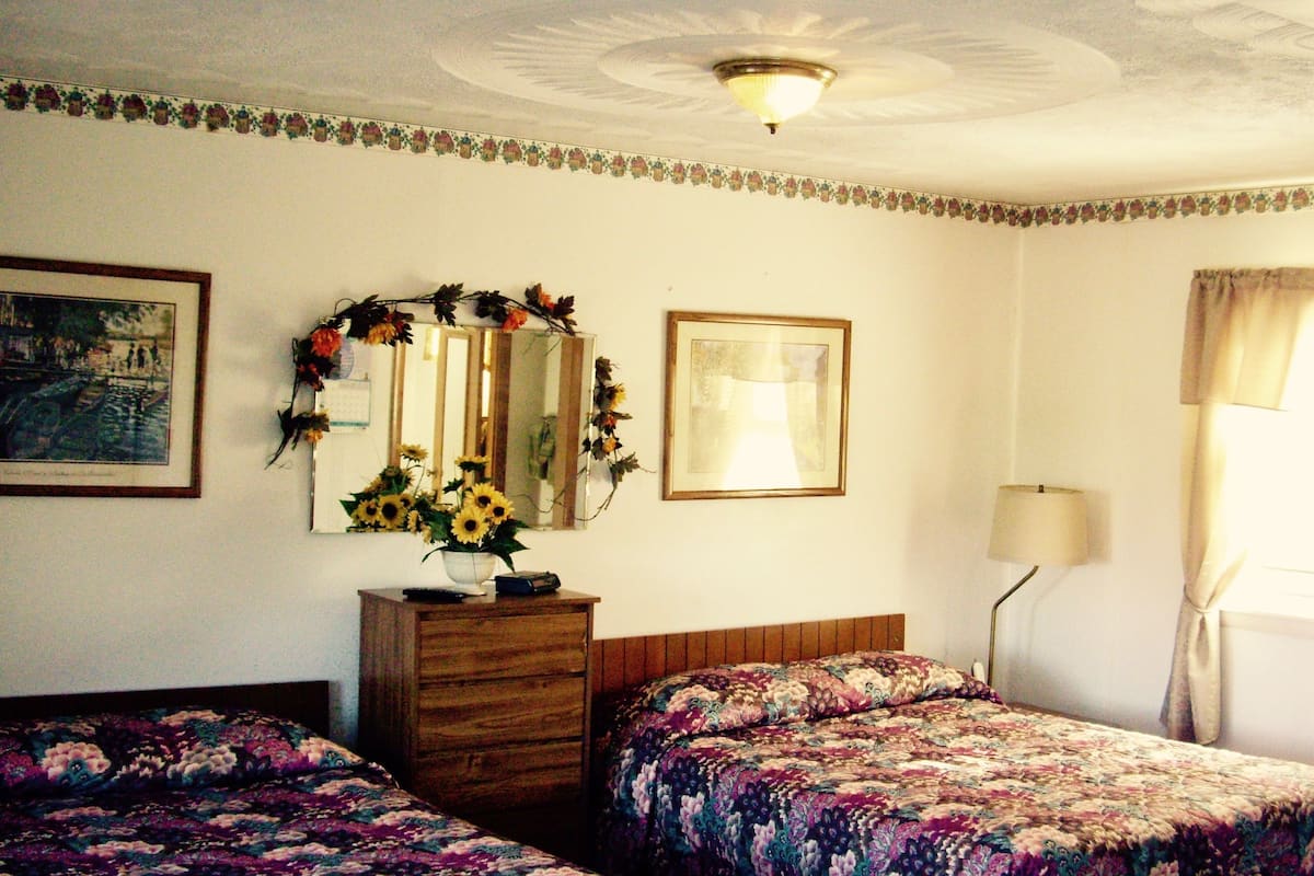 Ein Schlafzimmer mit zwei Betten, einem Schminktisch, einem Spiegel, einer Lampe und einem Fenster mit Vorhängen.