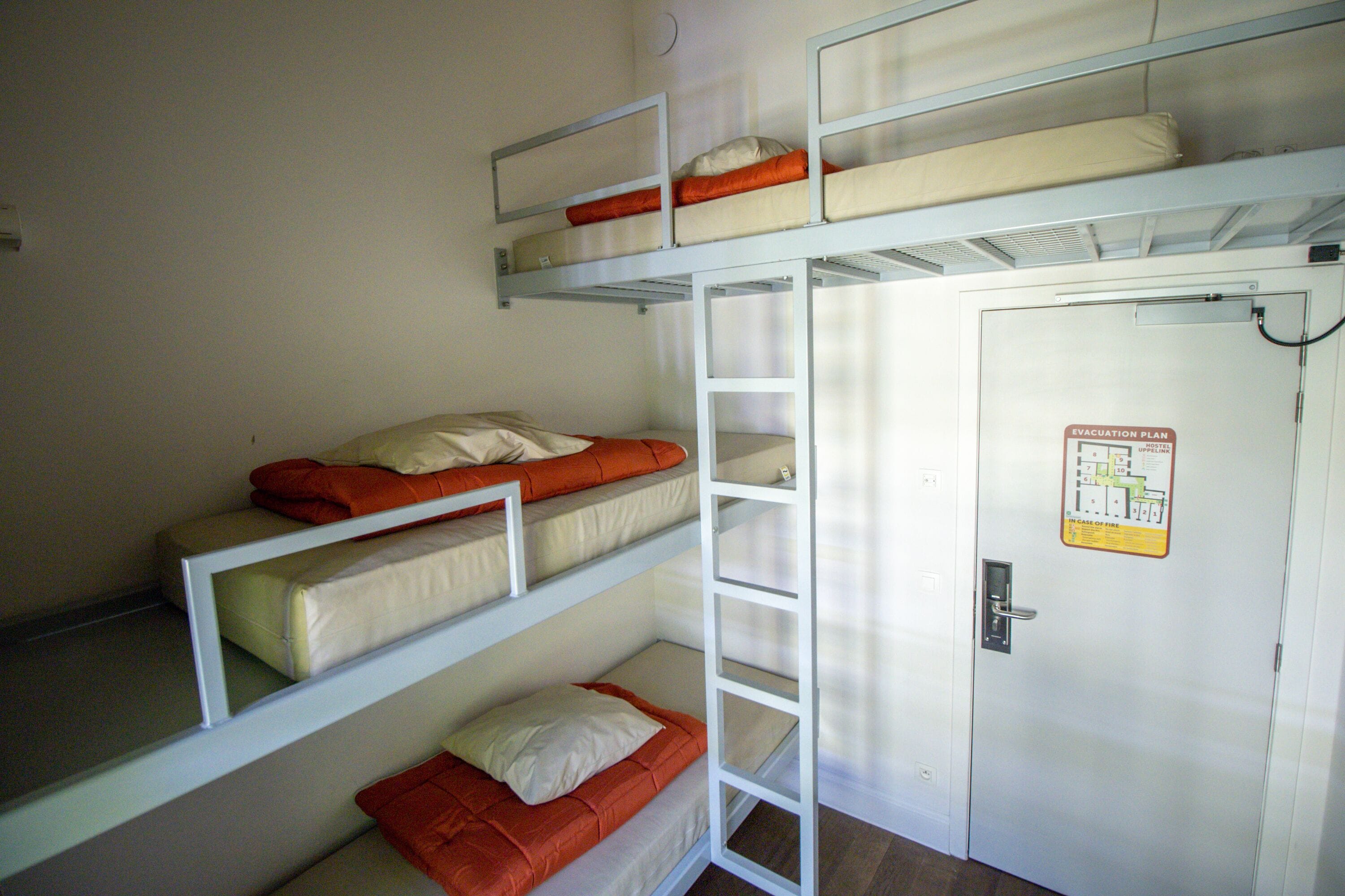 Une chambre avec un lit superposé, une porte et une affiche présentant le plan d’évacuation.