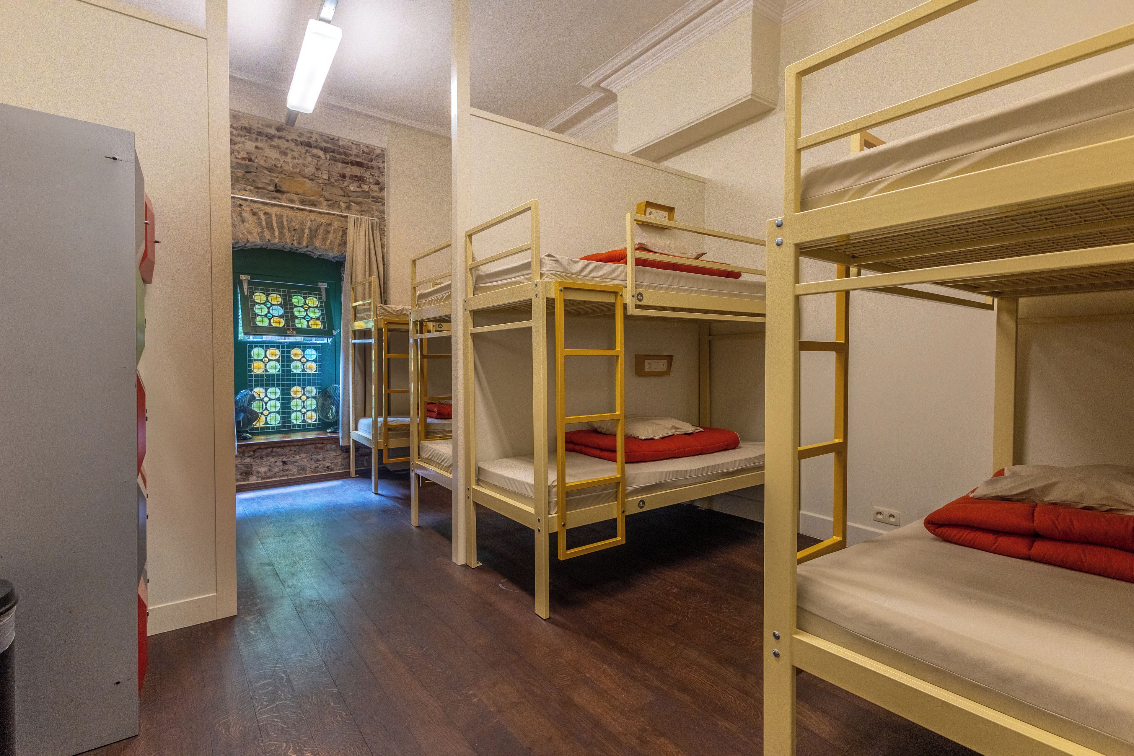 Ein Zimmer mit Etagenbetten, Holzboden, einer Tür und einem Fenster mit Buntglasdekor.