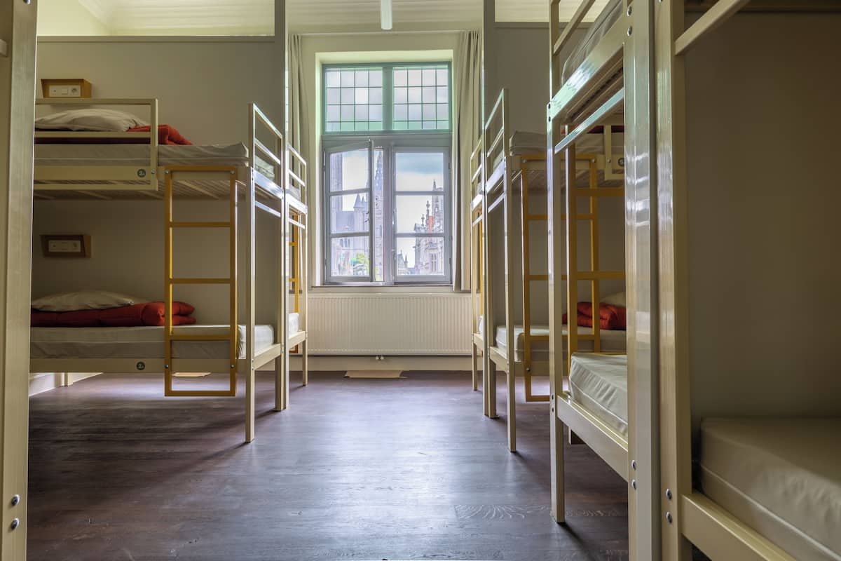 Um quarto de dormitório com beliches, uma janela com vista para edifícios e um radiador sob a janela.