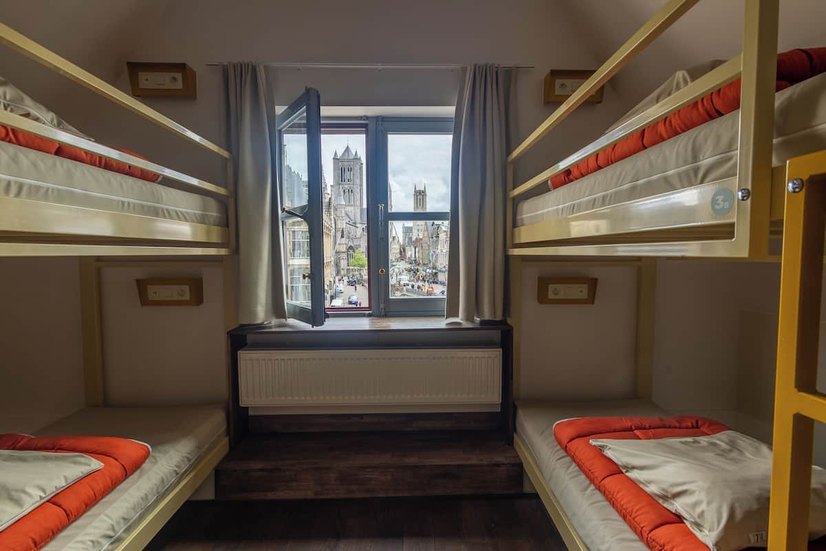 Quarto com beliches, vista para a cidade e janela com cortinas.