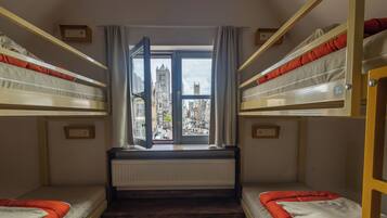 Ein Zimmer mit Etagenbetten, Blick auf eine Stadtlandschaft und einem Fenster mit Vorhängen.