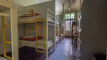 A room with bunk beds, a bathroom with a toilet and sink, and a window with a view of the outside.