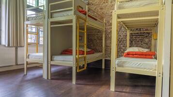 Une pièce avec trois lits superposés, un plancher en bois, un mur en briques et une fenêtre avec des rideaux.