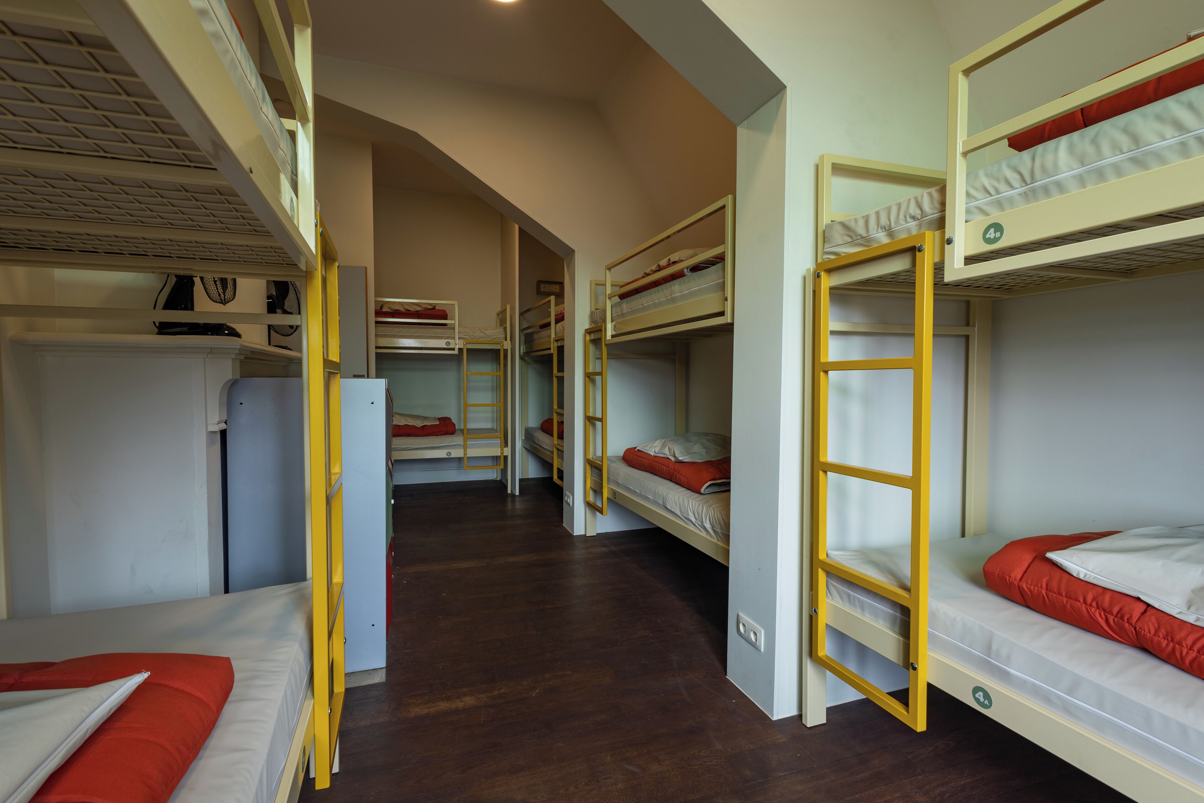 Un dormitorio con literas, pisos de madera y una pared blanca con ventana.