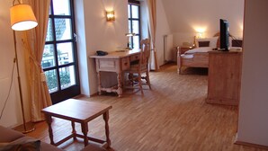 A room with a wooden floor, a desk, a chair, a bed, and a television. - Landhaus Sassenhof (Muelheim an der Ruhr)