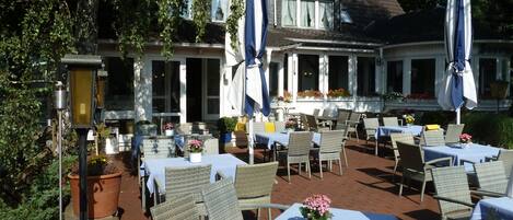 An outdoor seating area with wicker chairs and tables, potted plants, and umbrellas.