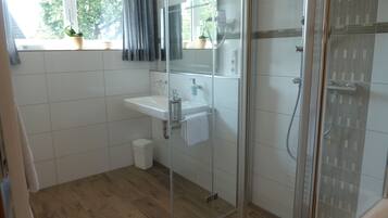 A modern bathroom with a glass shower enclosure, a white sink, and a wooden floor.